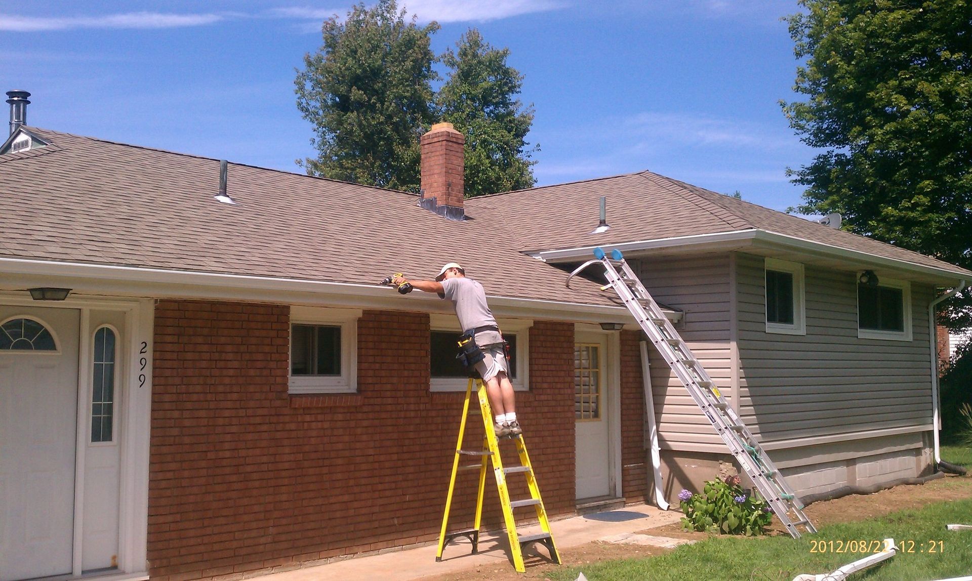 A man on a ladder paints the side of a house