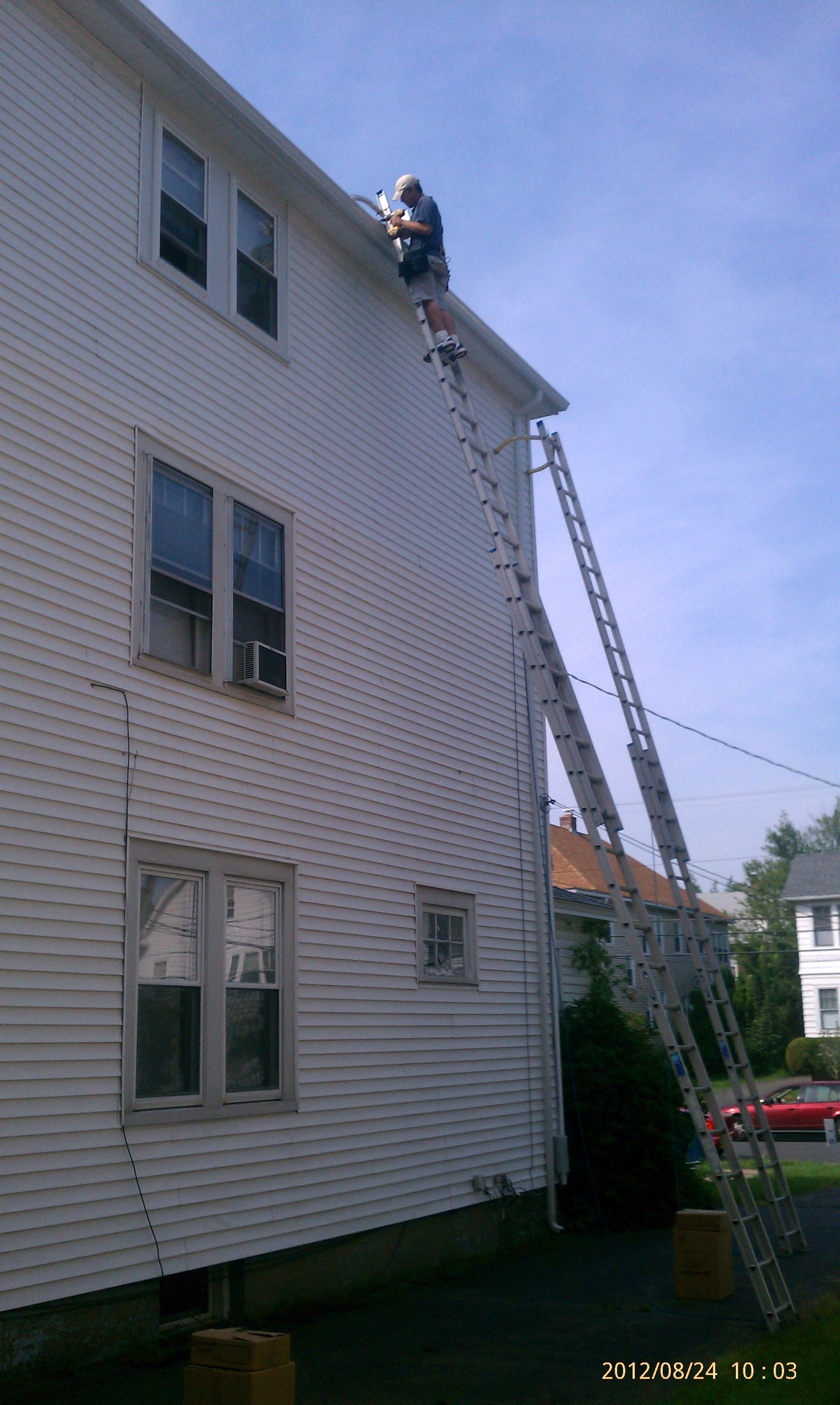 A man is standing on a ladder on the side of a house.