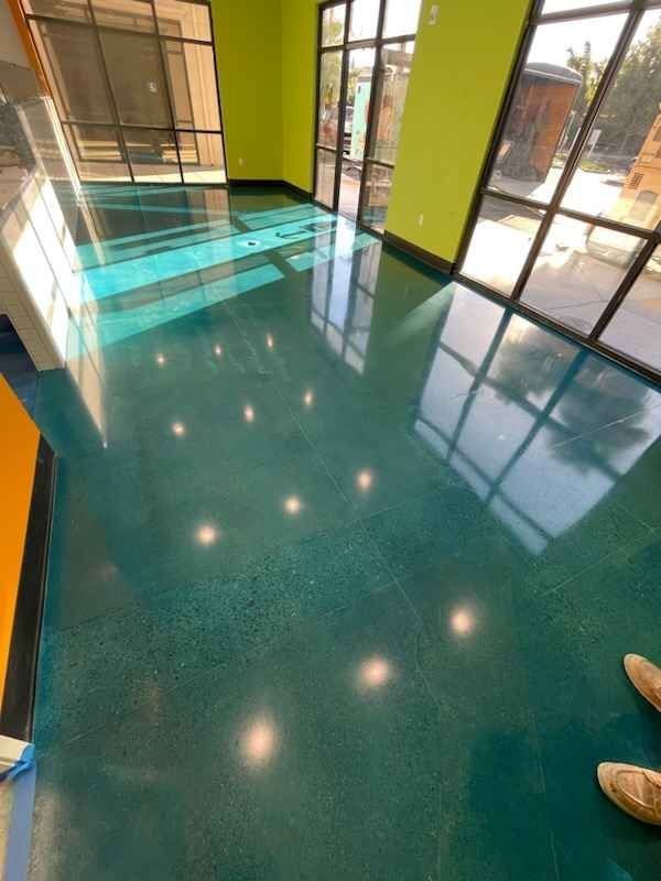 A person is standing on a shiny green concrete floor in a room with lots of windows.