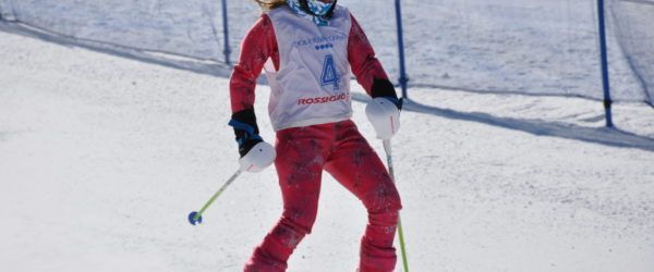 Skier in red suit and bib with number 4 skiing down a snowy slope.