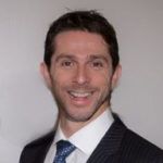 Man in suit smiles at the camera, against a white background.