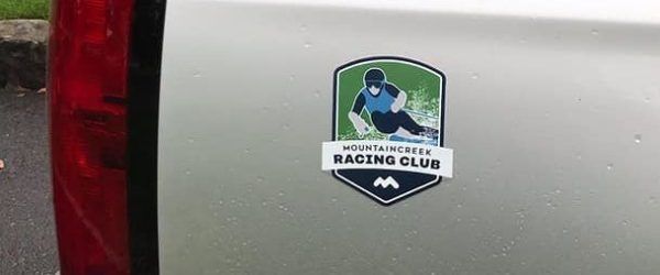 A silver car with a racing club sticker featuring a skier.