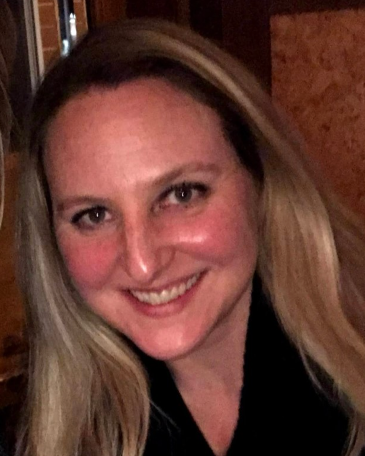 Man in a suit smiles, soft lighting from window behind.