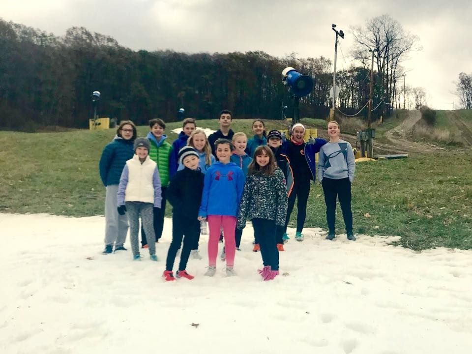 Group of kids in winter clothing stand in the snow near a slope.