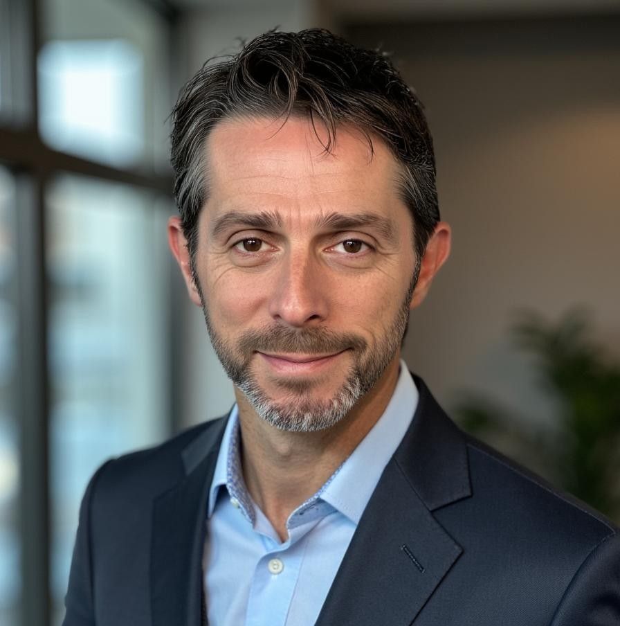 Man in a suit smiles, soft lighting from window behind.