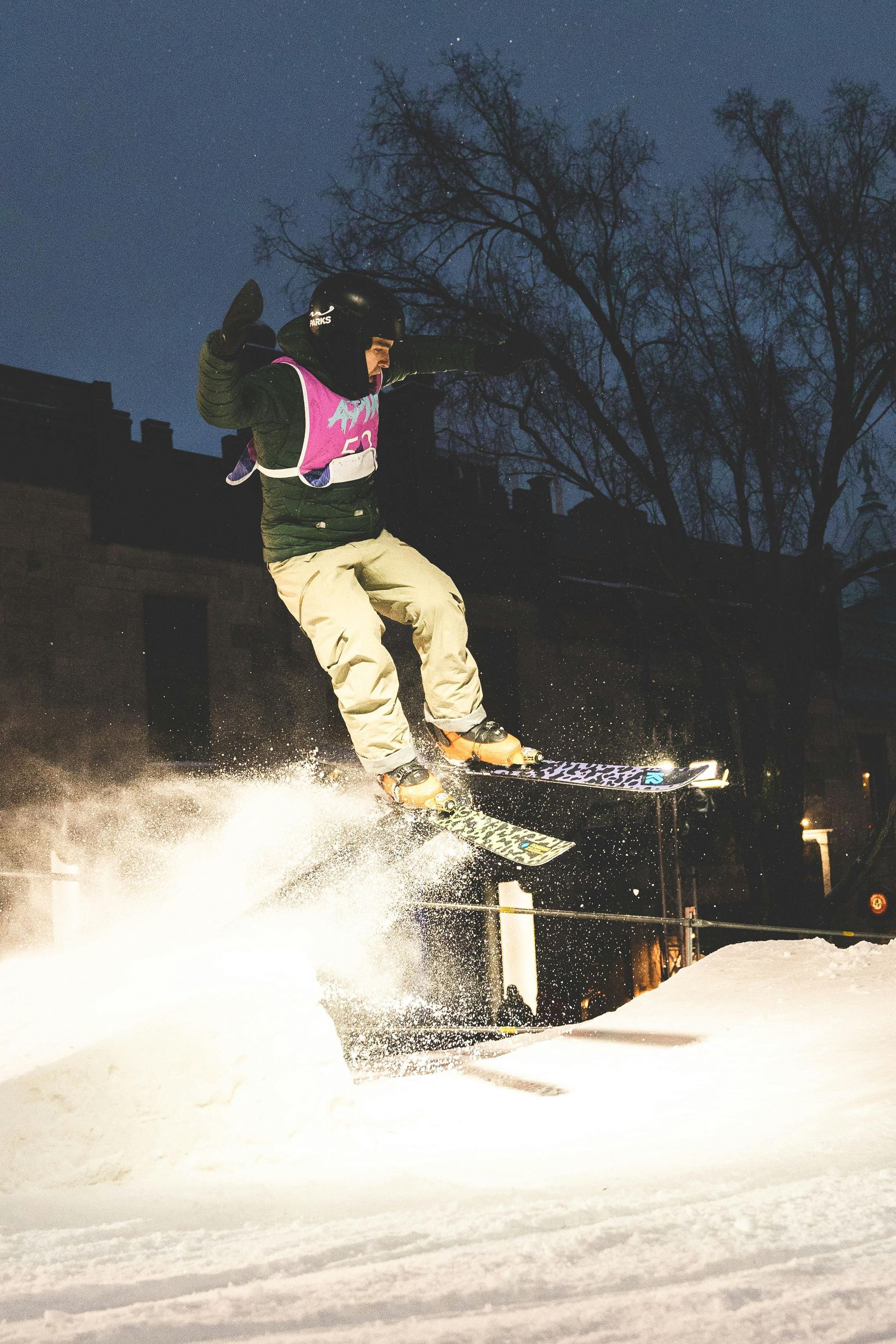Skier in mid-air performing a trick, night setting, snow flying up, lit up with head and body protection.