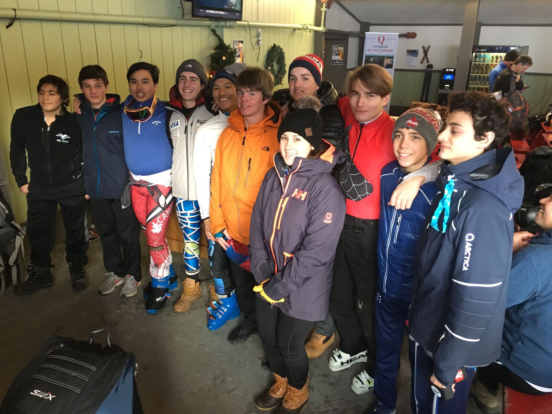 Group of skiers posing together indoors; some wearing ski gear, smiling.