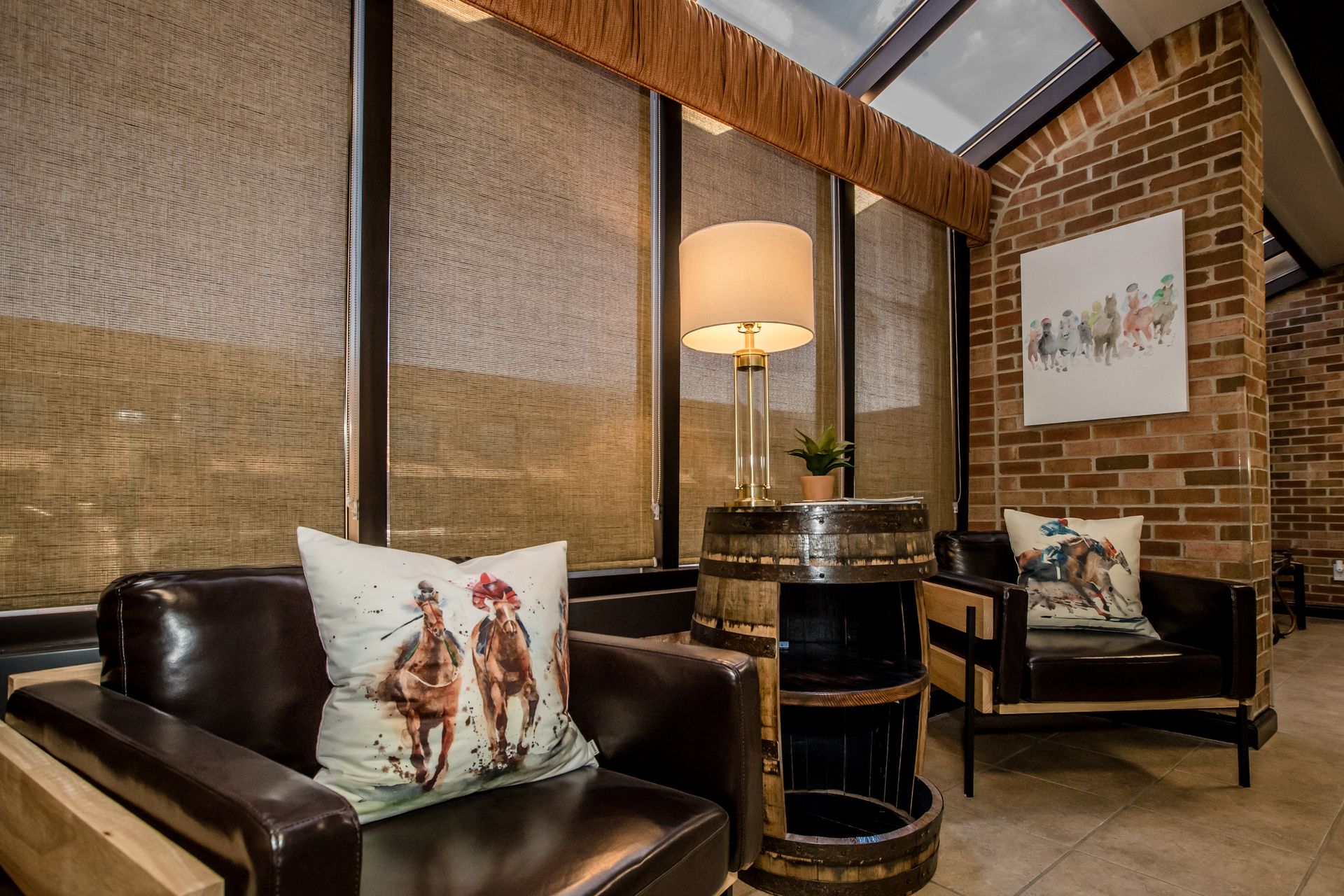 A living room with two chairs , a table , a lamp and a pillow with horses on it.