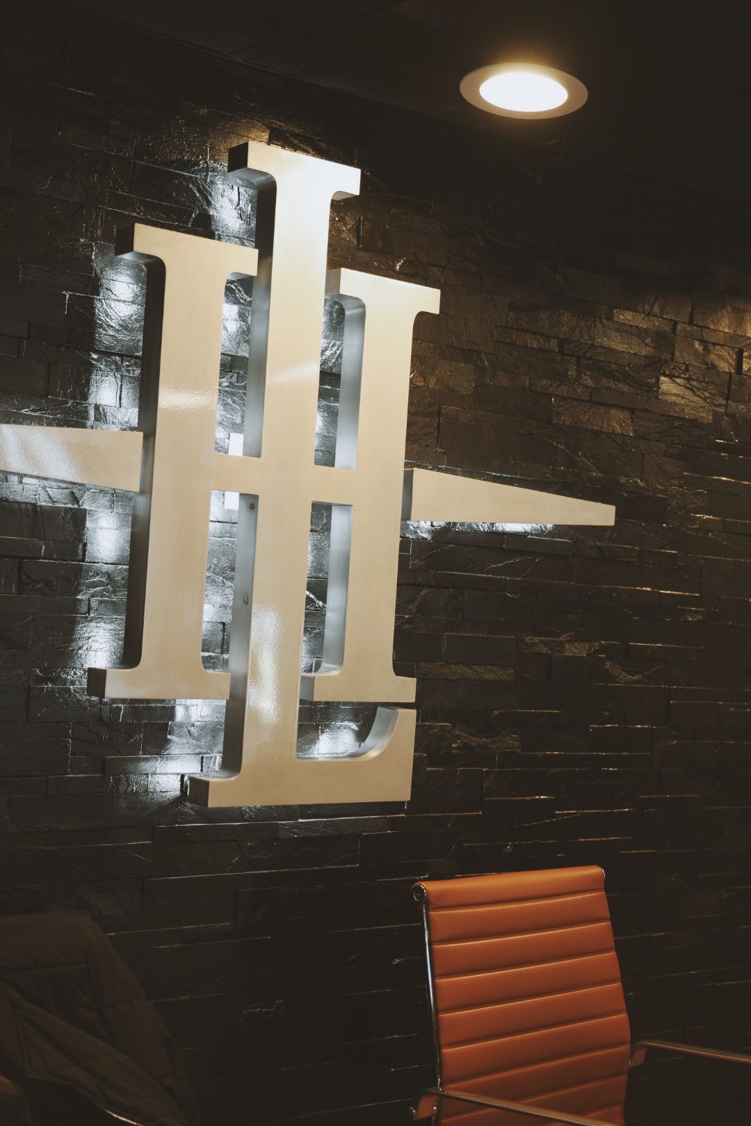 A chair is sitting in front of a brick wall with a large letter l on it.