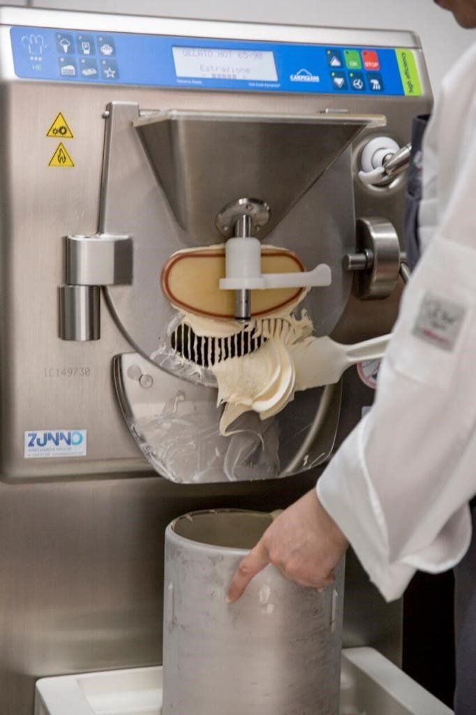 Una persona che estrae il gelato da una macchina commerciale e lo versa in un contenitore.