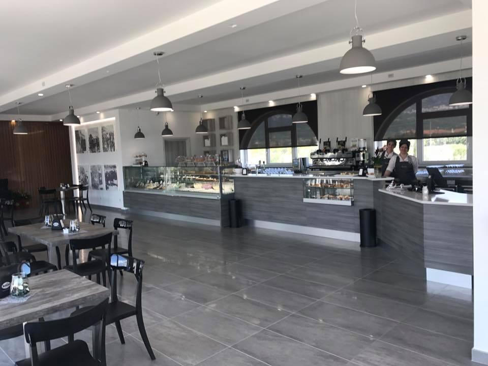 Interno di un bar moderno nei toni del grigio. Tavoli, sedie, bancone con pasticcini e personale.