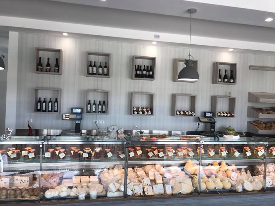 Interno di un negozio di formaggi con vetrine, scaffali per il vino e illuminazione dall'alto.