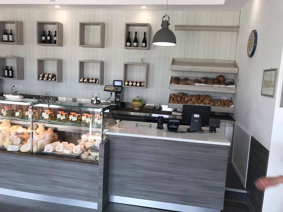 Interno di un panificio con vetrine, scaffali con prodotti, bancone e illuminazione dall'alto.