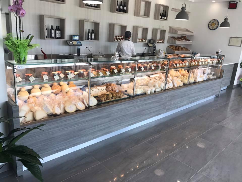 Un espositore con vari formaggi e cibi pronti. Una persona è in piedi dietro il bancone e serve i clienti.