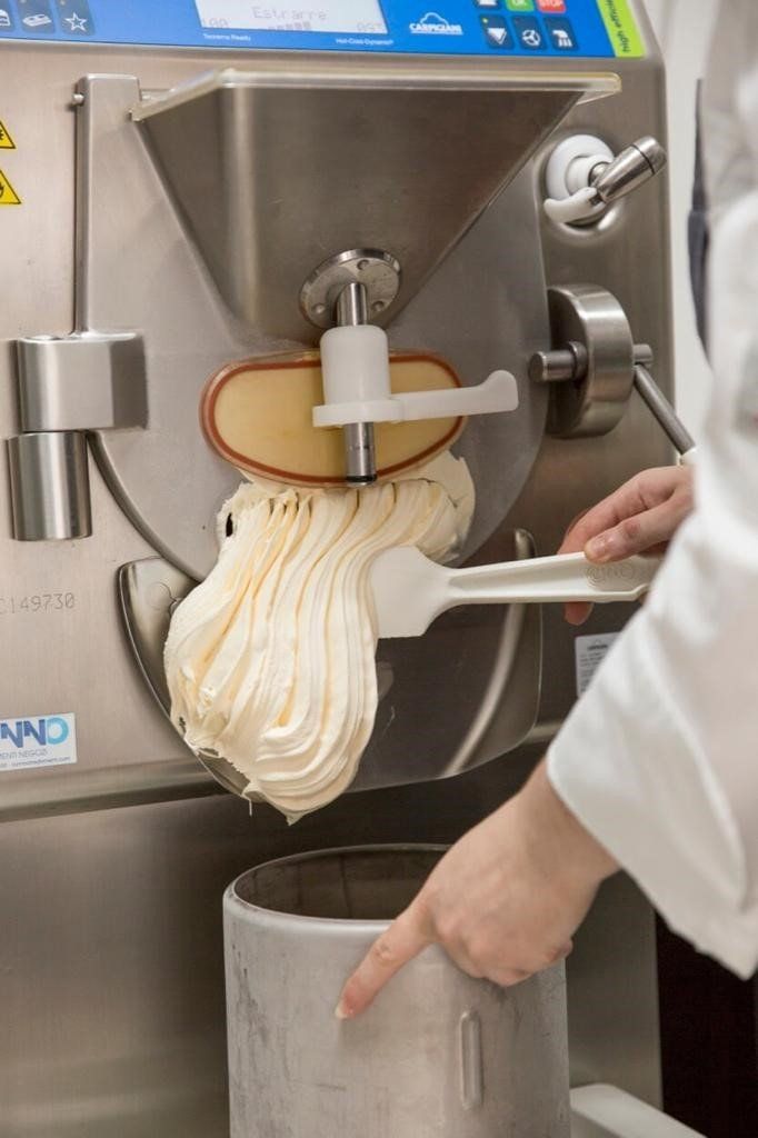 Una gelatiera eroga il gelato soft in un contenitore metallico; una persona usa una spatola per guidarlo.