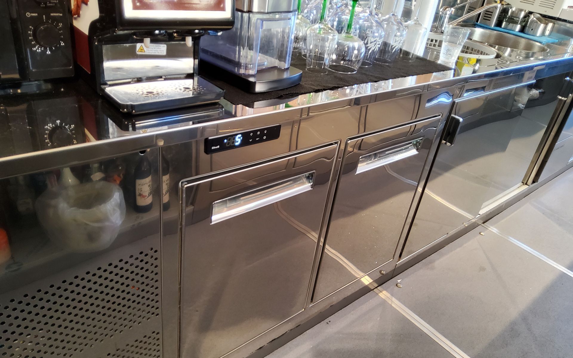 Frigorifero commerciale in acciaio inox sotto il bancone del bar, con macchina per il caffè a vista.