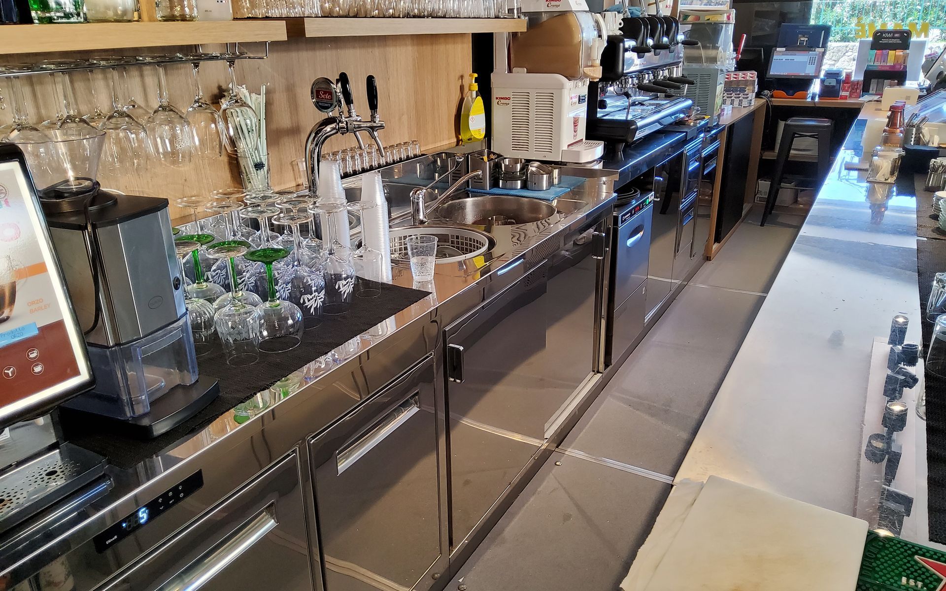 Interno del bar con banconi, bicchieri ed elettrodomestici in acciaio inossidabile.