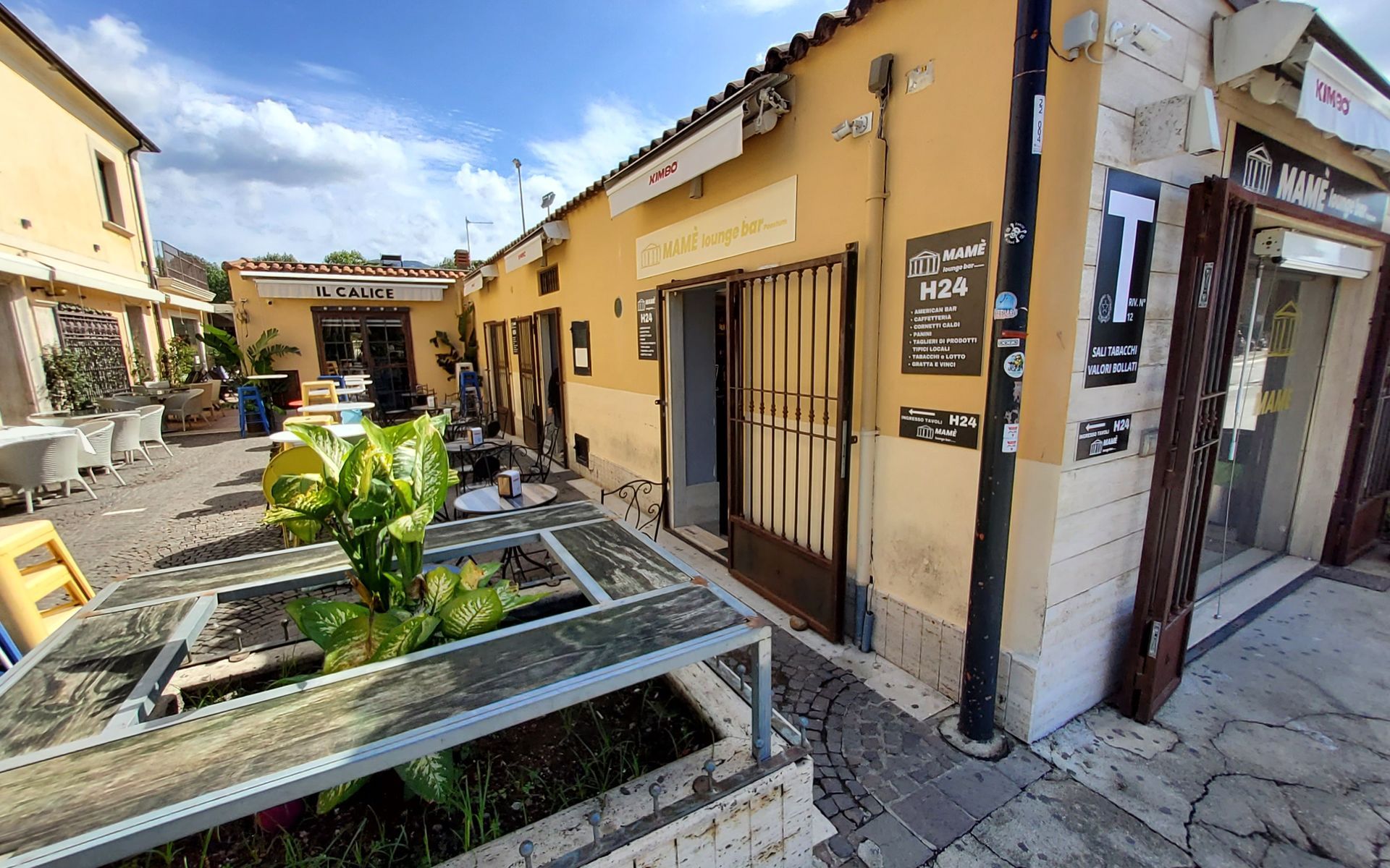 Cortile con edifici gialli, un cancello metallico e posti a sedere all'aperto.