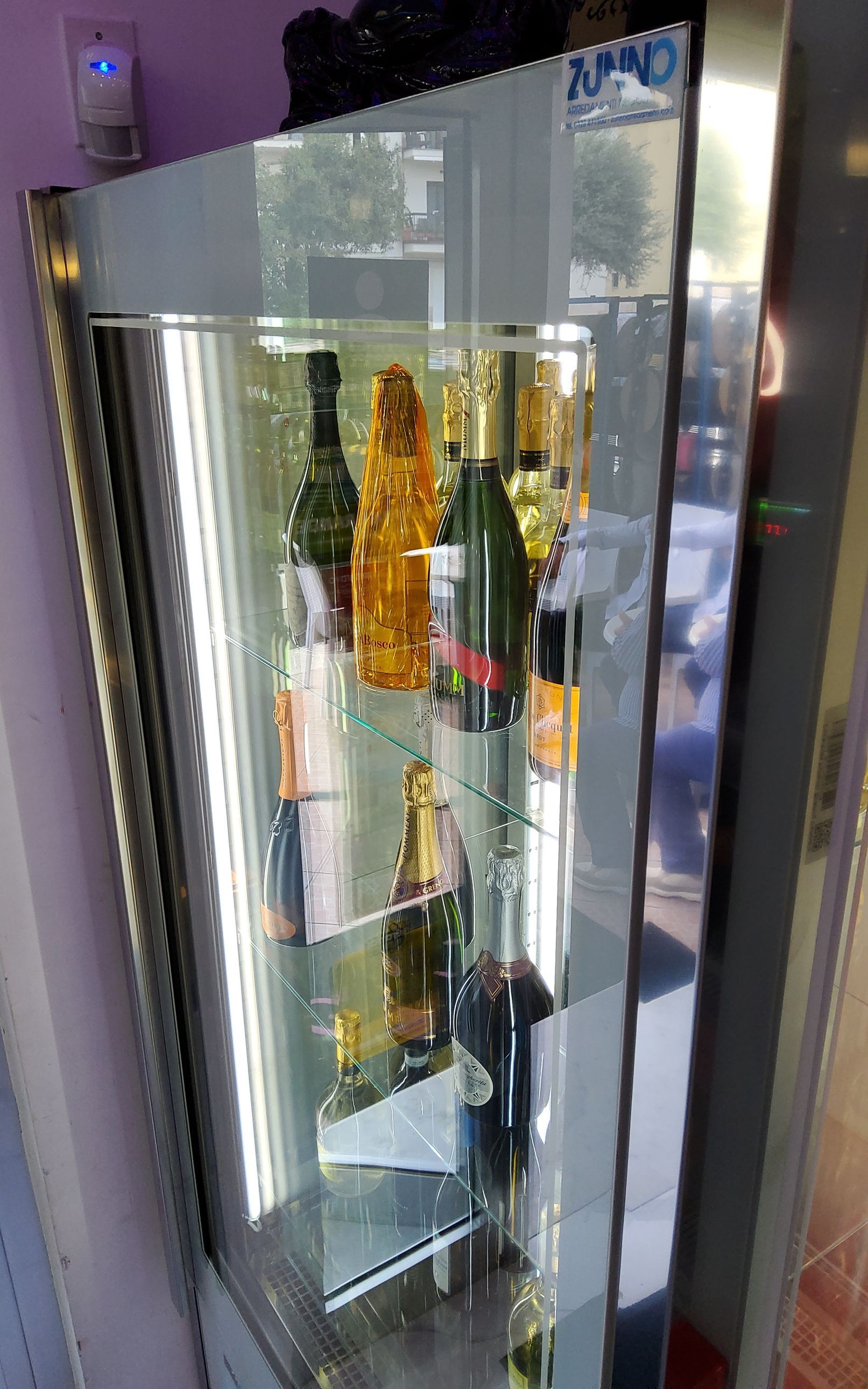 Vetrina con bottiglie di champagne, finiture in argento e ripiani in vetro.