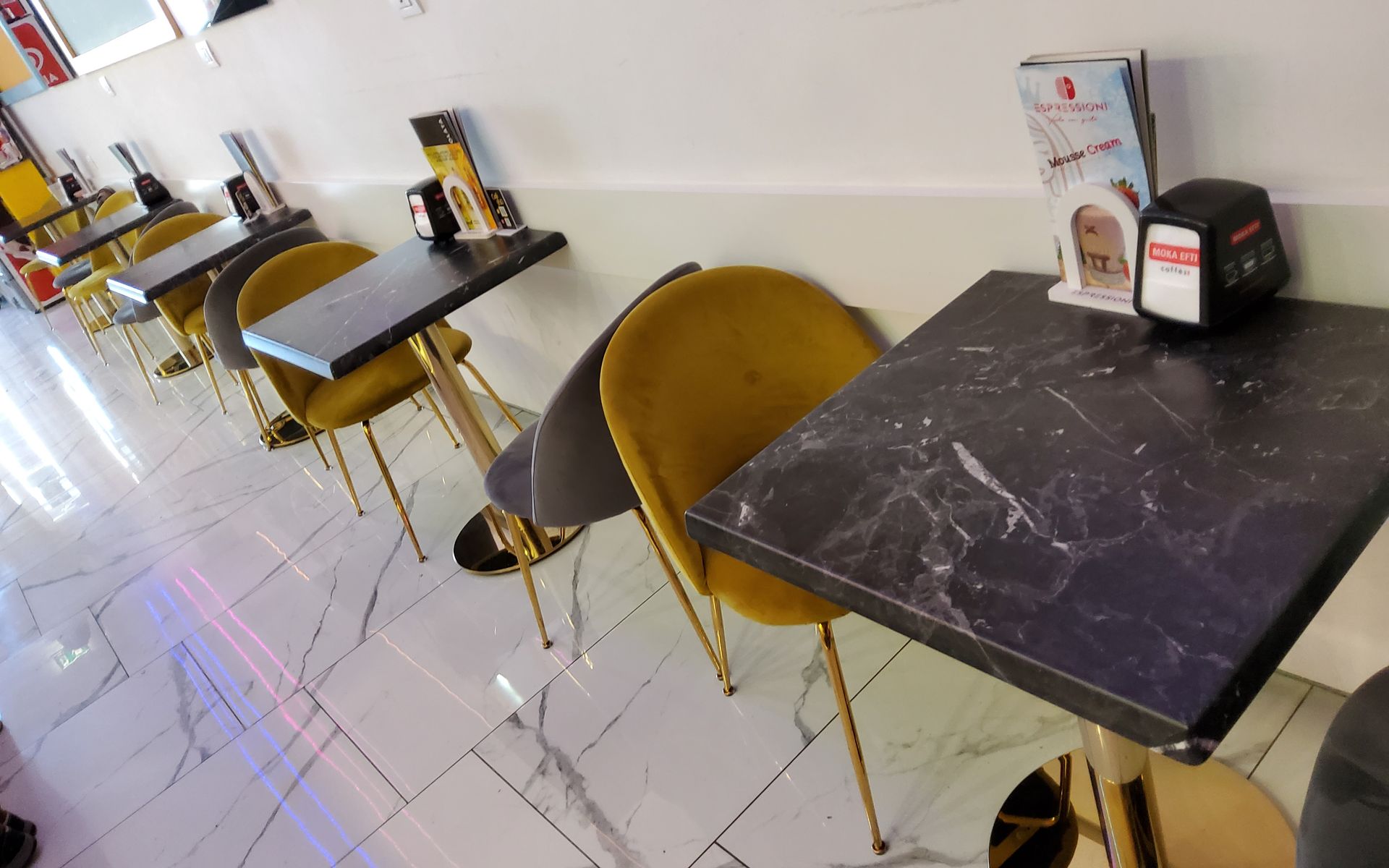 Interno del bar con tavoli in marmo nero, sedie dorate e menu.