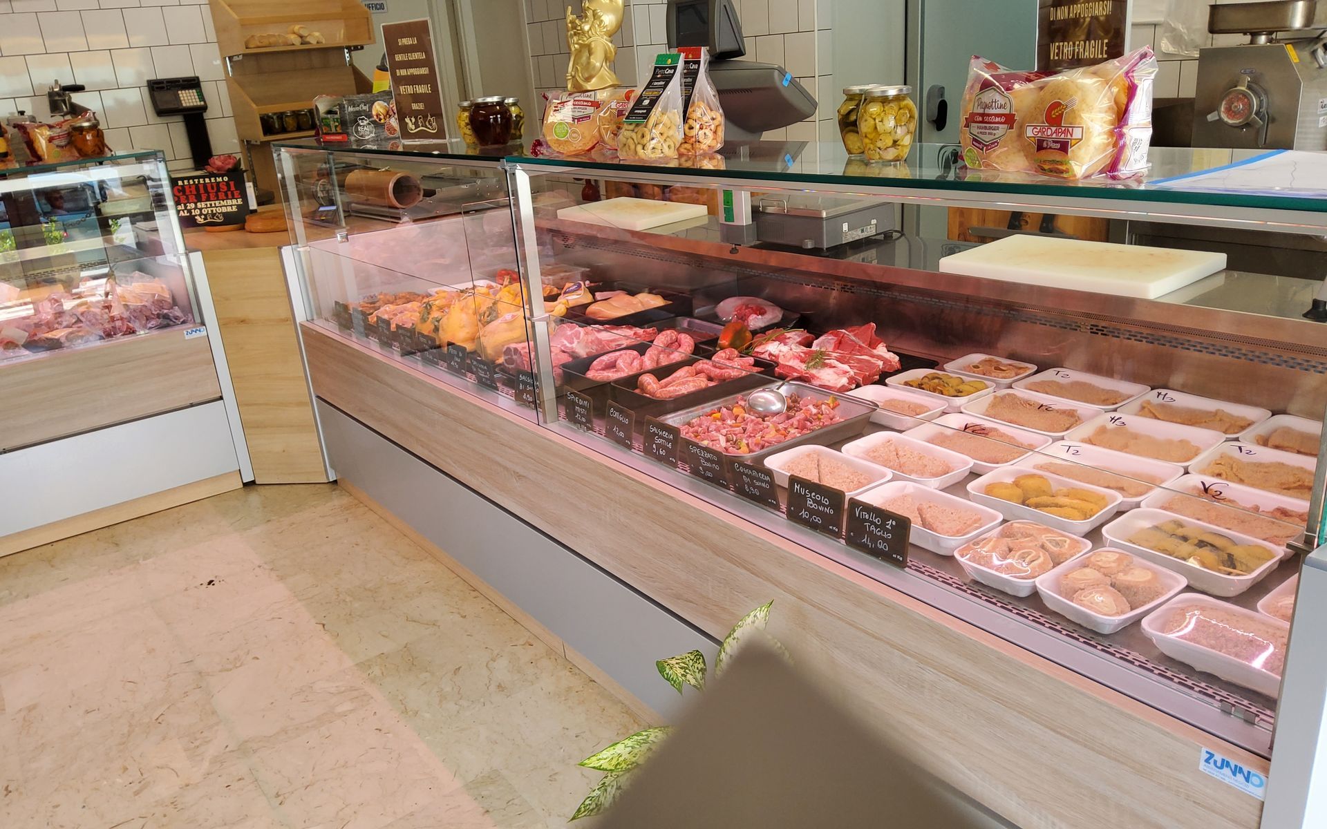 Una vetrina refrigerata per la carne in un negozio, piena di vari tagli di carne e cibo preparato.