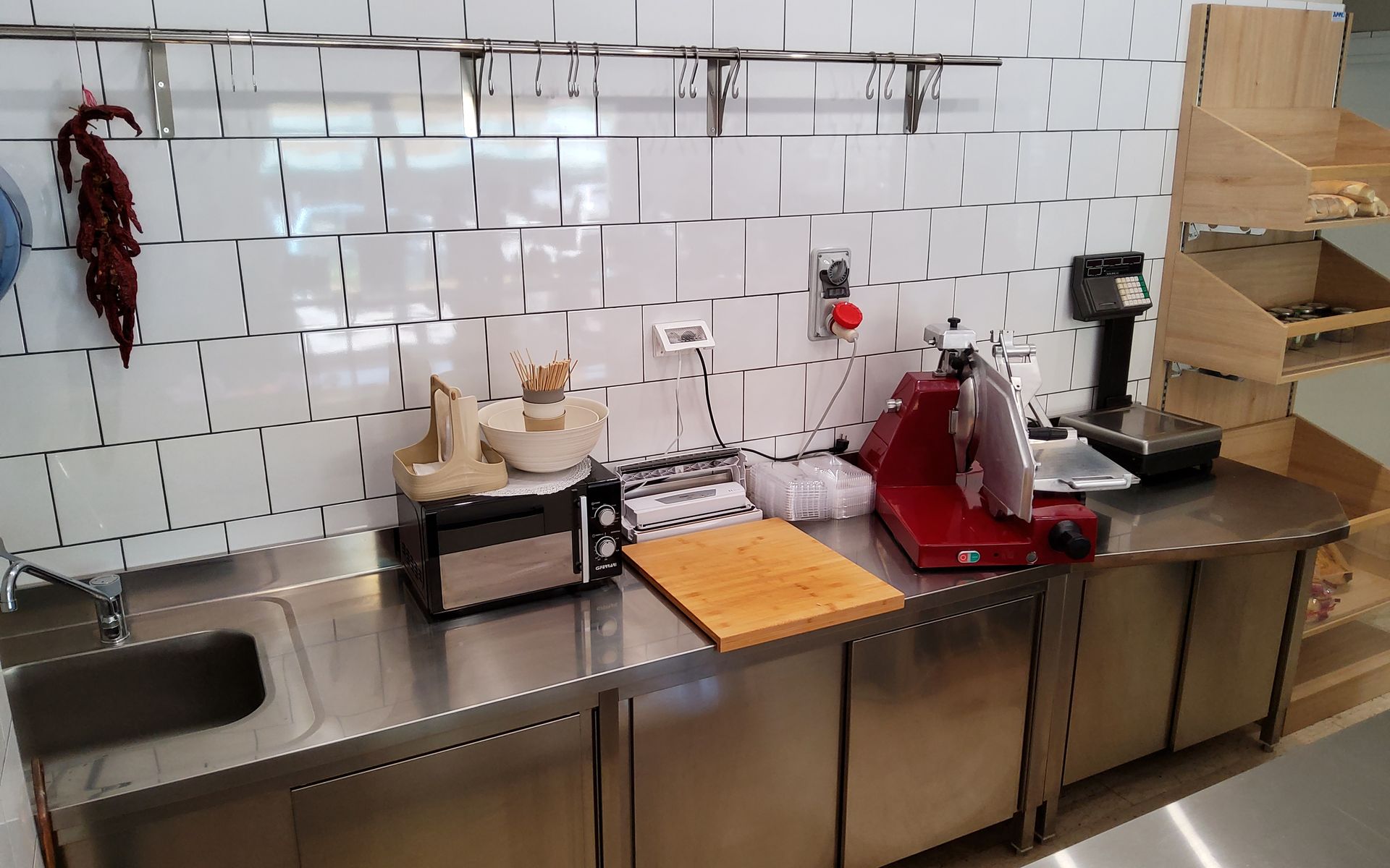 Cucina in acciaio inossidabile con paraschizzi piastrellato bianco, elettrodomestici, tagliere e ripiani.