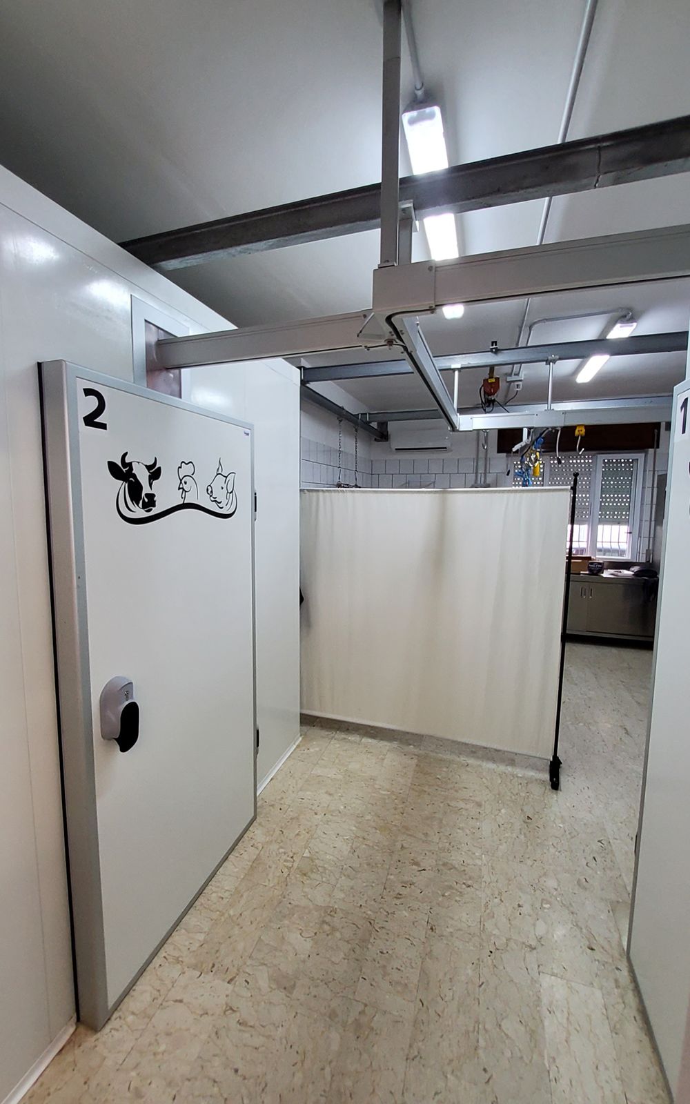 Corridoio di una clinica veterinaria con porte, box e luci a soffitto bianchi. Numero 2 sulla porta con adesivo raffigurante un animale.