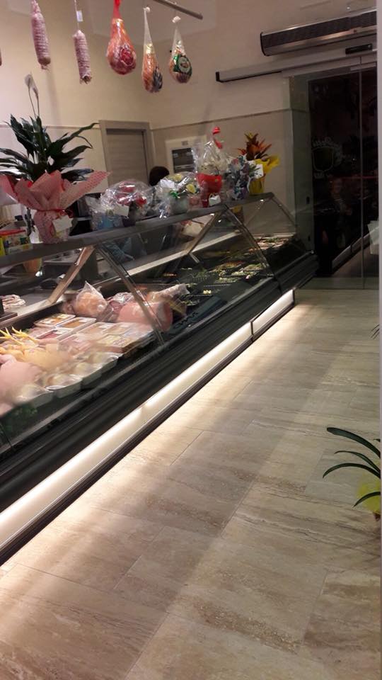 Un bancone di gastronomia con vari prodotti alimentari in esposizione, illuminato da una striscia di luce.