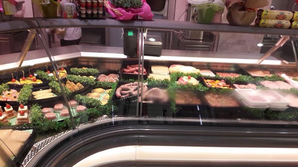 Un banco refrigerato di gastronomia pieno di vari alimenti preparati, tra cui carni e formaggi, in un negozio.