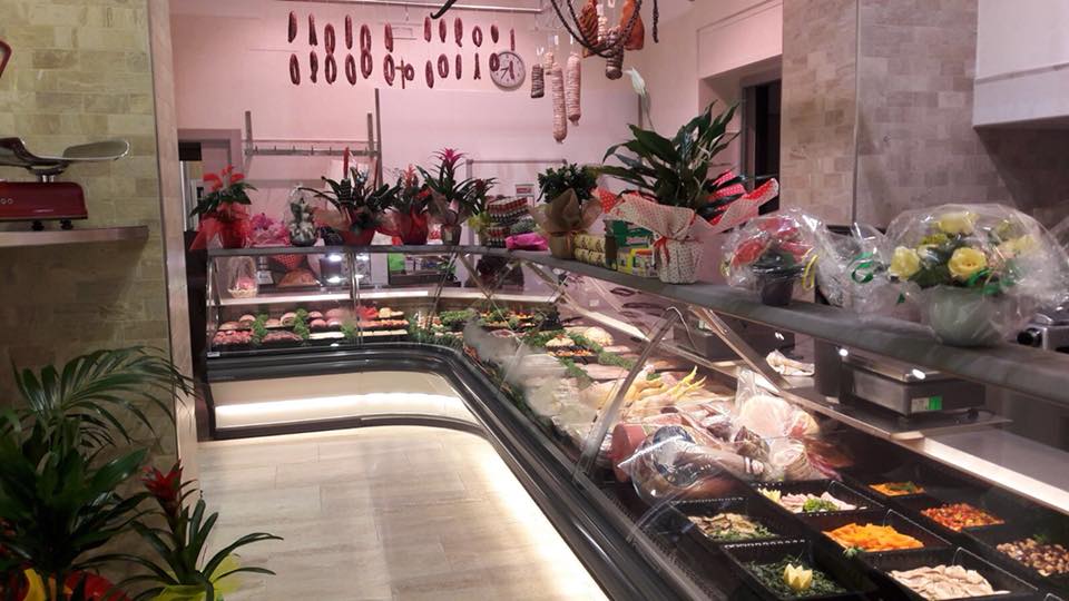 Interno di una macelleria con vetrine di carni, fiori e cibi preparati.