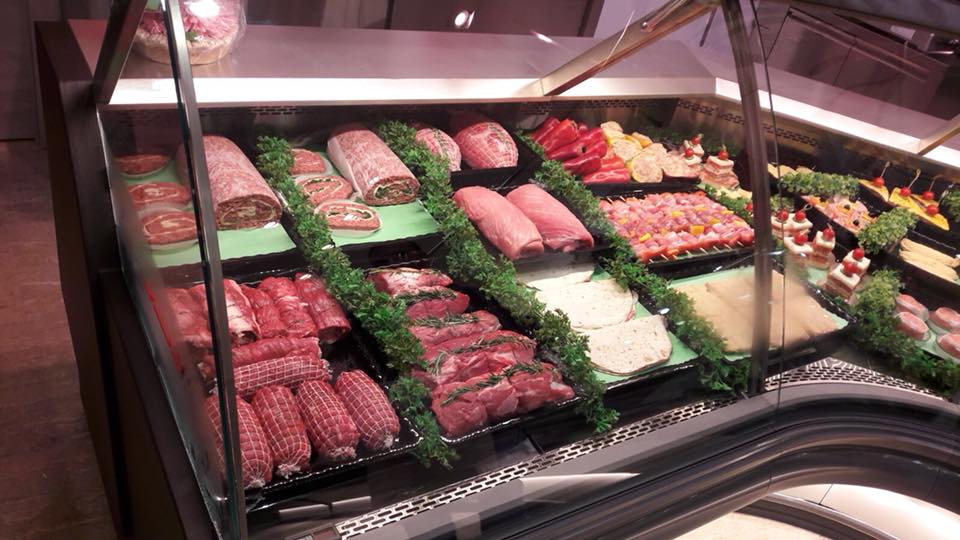 Vetrina di una macelleria piena di vari tagli di carne, salsicce e cibi preparati.