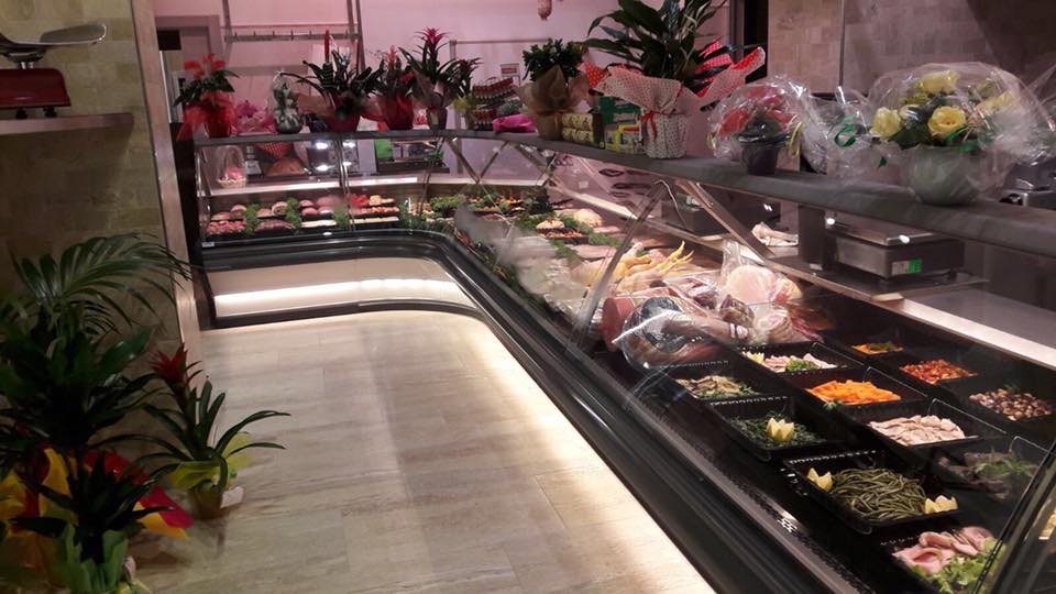 Una vetrina gastronomica piena di cibi preparati; le piante decorano lo sfondo e il bancone.