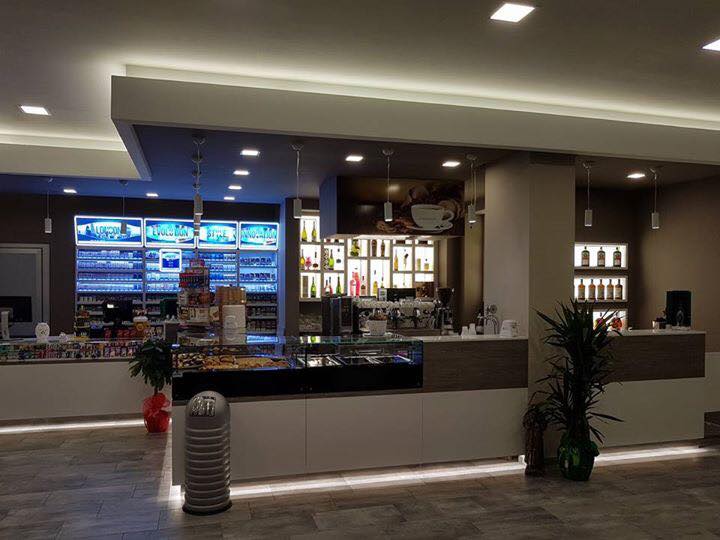 Vista interna di un bar con bancone, vetrine e scaffali con prodotti.