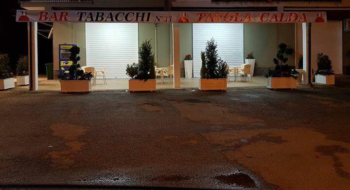Bar e caffetteria di notte con le persiane chiuse, le piante nei vasi e il pavimento bagnato.