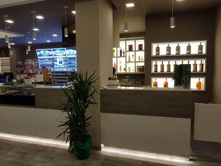 Interno di un bar, con il bancone su cui sono esposte le bottiglie di liquore. Pianta verde in primo piano.