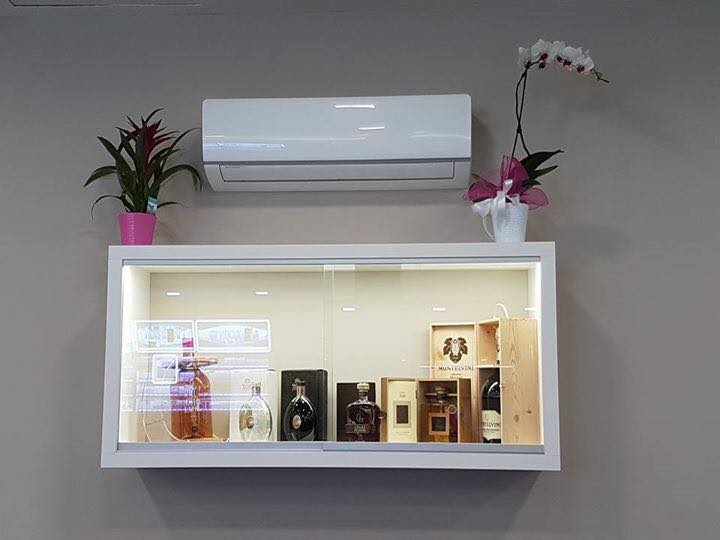 Vetrina bianca con bottiglie e condizionatore sopra, piante sopra.