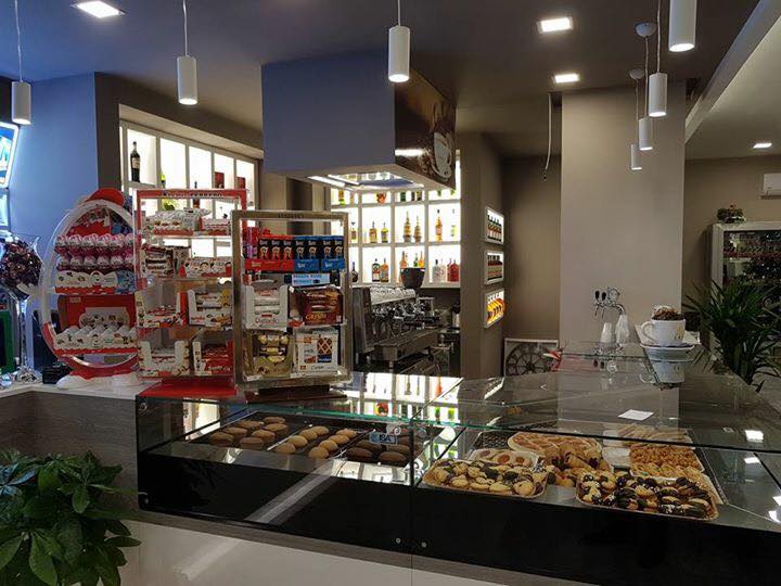L'interno di un bar con dolci in esposizione, un bancone e scaffali pieni di bevande e snack.