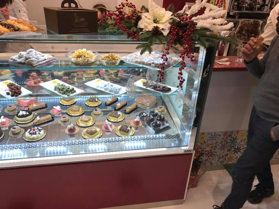 Vetrina piena di pasticcini e una persona in piedi accanto.