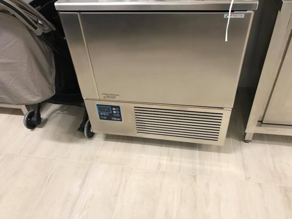 Macchina per il ghiaccio commerciale in acciaio inossidabile appoggiata a una parete su un pavimento piastrellato.