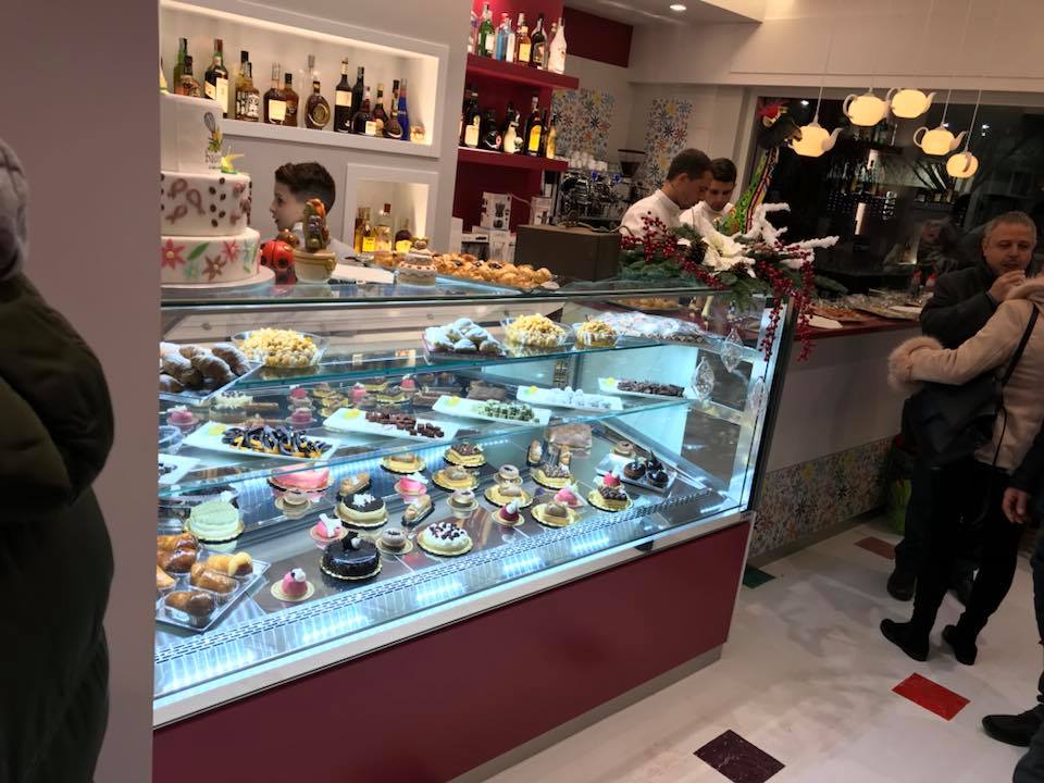 Una persona è in piedi vicino all'espositore di una pasticceria. Il negozio offre torte, pasticcini, un bar e personale.