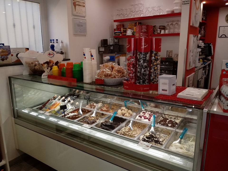 Vetrina di una gelateria con vari gusti di gelato, dietro un bancone in vetro.