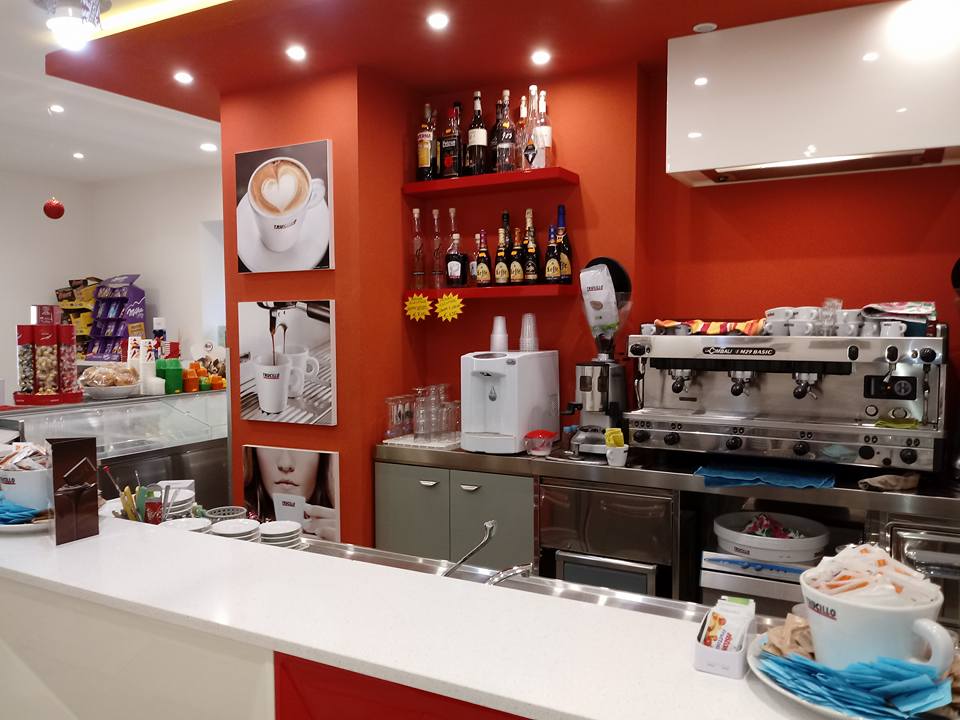Interno di una caffetteria con macchina per l'espresso, bar, bevande e pareti rosse e bianche.