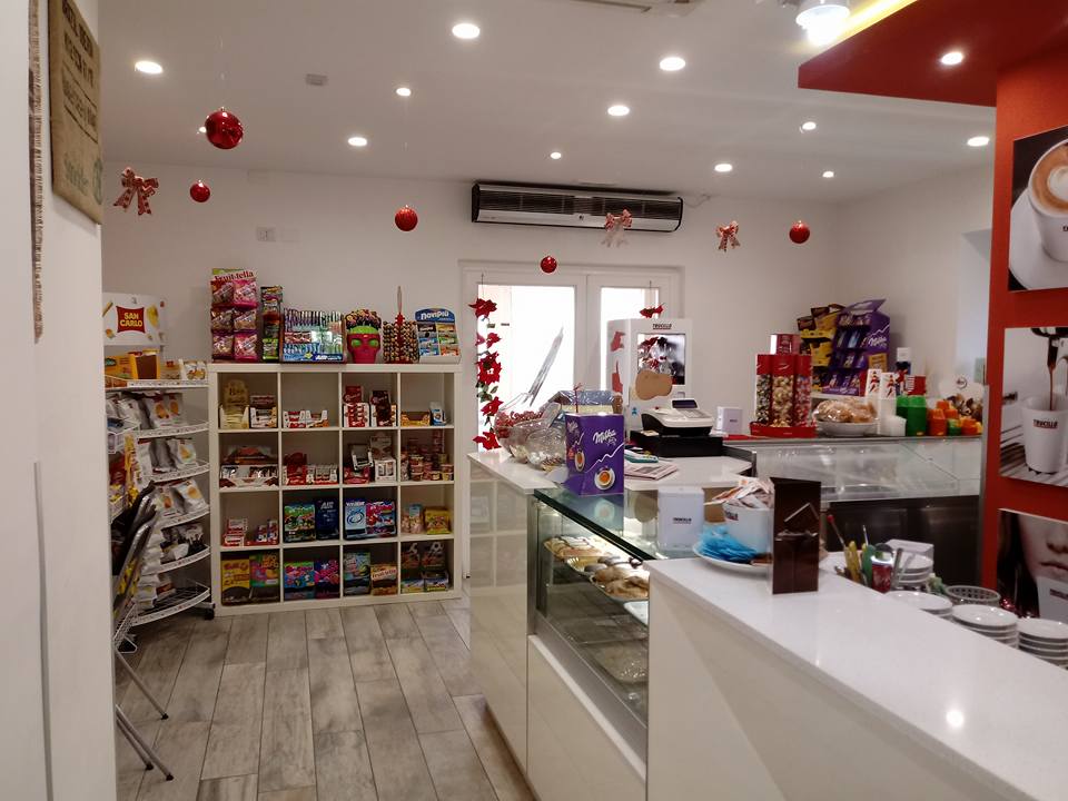 All'interno di un piccolo negozio: bancone bianco, scaffali di snack, decorazioni rosse.