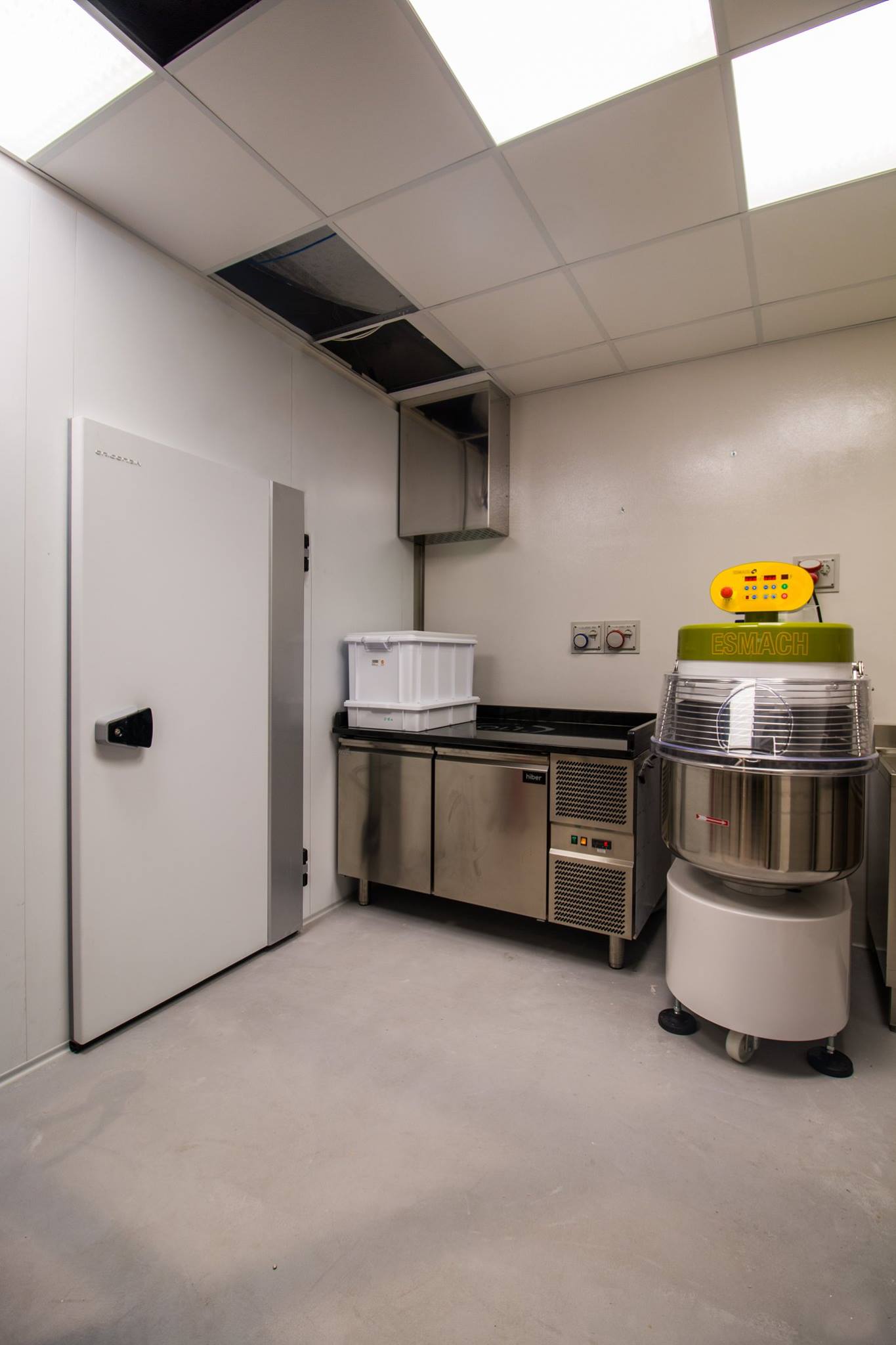 Interno di una cucina commerciale con cella freezer, mobili in acciaio inossidabile e attrezzature per la lavorazione degli alimenti.