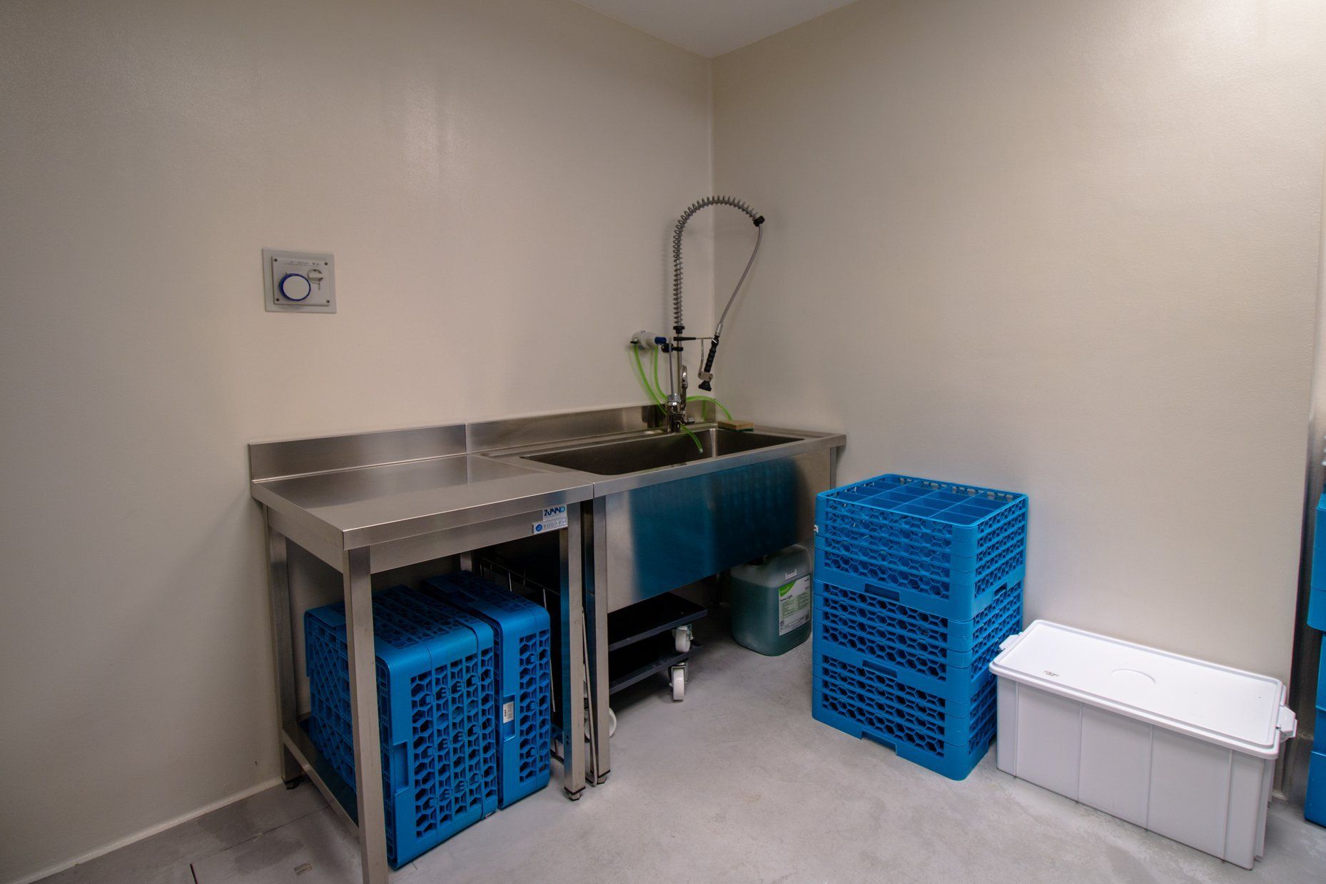 Un lavello in acciaio inossidabile in un angolo della stanza, con scolapiatti blu e un contenitore bianco.