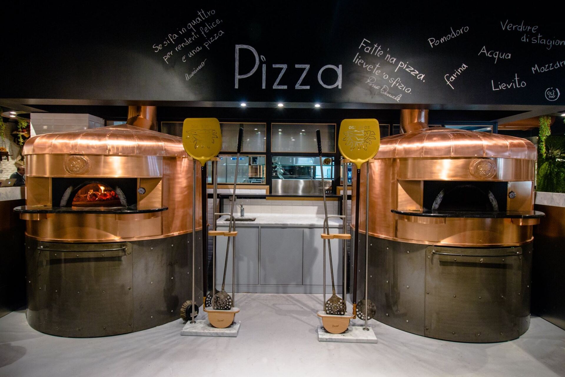 Due forni per pizza in rame con fiamme, pale per pizza e l'insegna