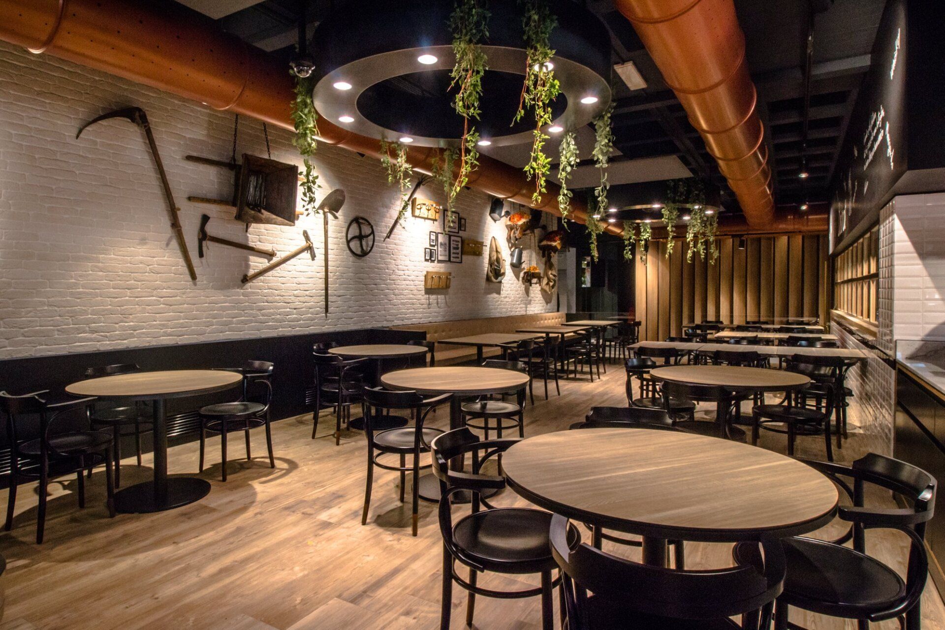 Interno di un ristorante con tavoli rotondi, sedie nere e utensili decorativi da parete.