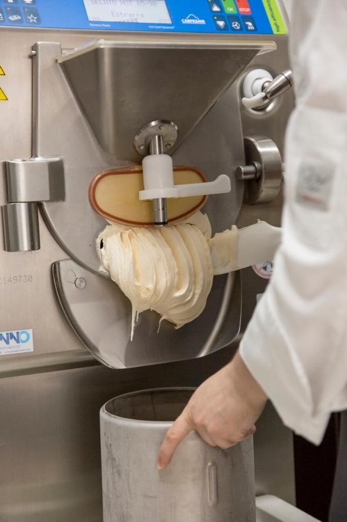 Persona che versa il gelato da una macchina in un contenitore d'argento.
