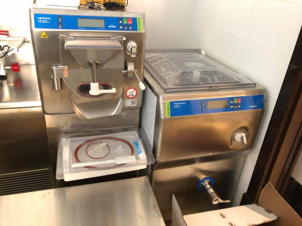 Due macchinari industriali in acciaio inossidabile, probabilmente destinati alla ristorazione, contro una parete piastrellata.