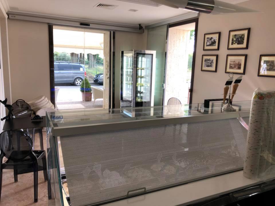 Interno di un bar con bancone, vetrina e porta aperta sull'esterno.